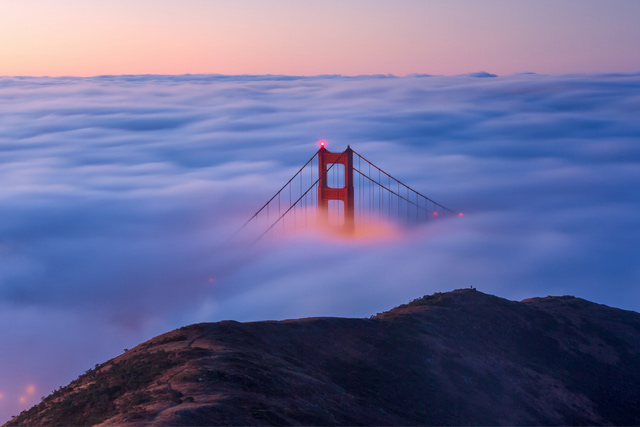 Fog layer filling San Francisco Bay as parts of the Golden Gate Bridge raise above the fog